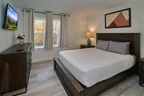 A bedroom with a bed, a nightstand, a lamp, a dresser, a TV, and a window with curtains. - The Ruby 115 (Pigeon Forge)
