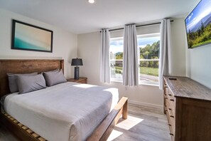 A bedroom with a bed, a nightstand, a lamp, a dresser, a window with curtains, and a painting on the wall. - The Ruby 200 (Pigeon Forge)