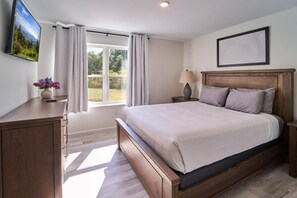 Een slaapkamer met een bed, een bureau, een lamp, een fotolijstje en een raam met gordijnen.