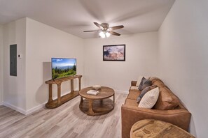 Een woonkamer met een televisie, een plafondventilator, een houten salontafel, een bruine bank en een lijst met een foto aan de muur.
