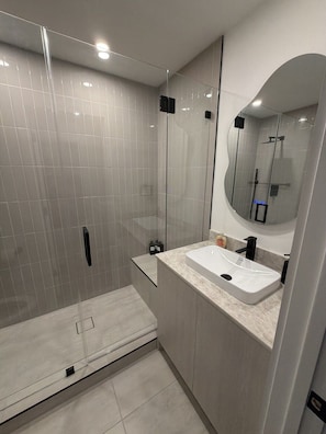 Une salle de bain moderne avec une douche à parois de verre, un lavabo avec un miroir et des murs carrelés.