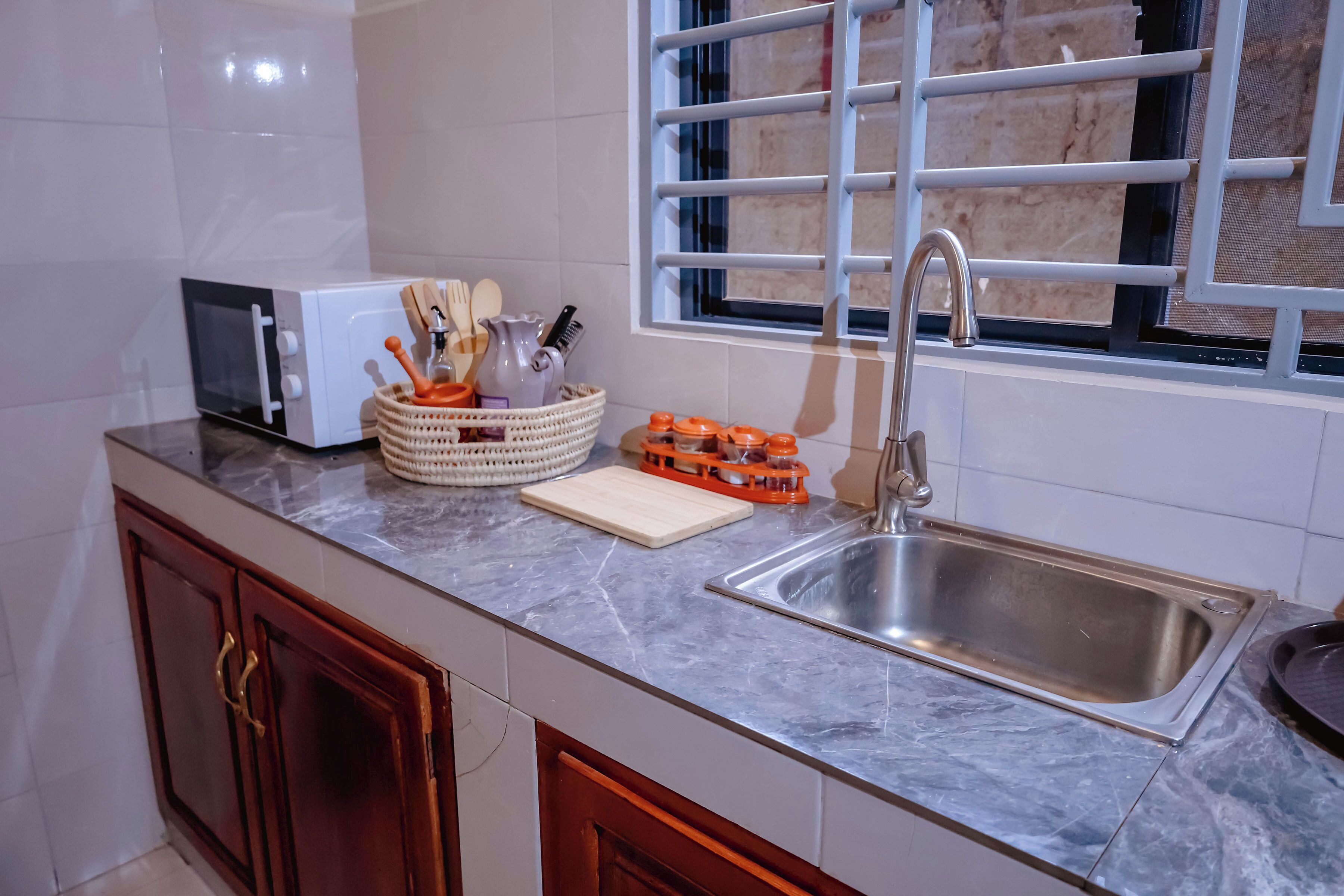 A kitchen with a microwave, sink, and window with bars.