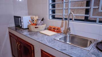 A kitchen with a microwave, sink, and window with bars.