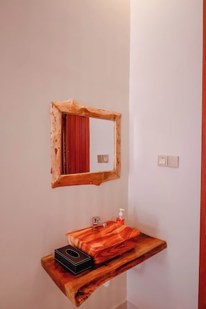 Een houten spiegel boven een houten wastafelmeubel, met een rode handdoek en een zeepdispenser.