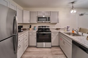 A modern kitchen with stainless steel appliances, a granite countertop, and light-colored cabinetry. - The Ruby 201 (Pigeon Forge)