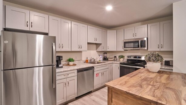A modern kitchen with stainless steel appliances, white cabinetry, and a wooden countertop. - The Ruby 202 (Pigeon Forge)