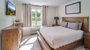 A bedroom with a bed, a nightstand, a dresser, a window with curtains, and a wall-mounted picture. - The Ruby 202 (Pigeon Forge)