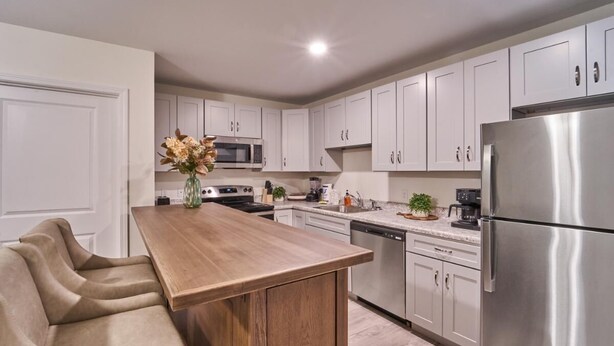 A modern kitchen with white cabinets, a stainless steel refrigerator, a wooden island, and a seating area with a sofa. - The Ruby 203 (Pigeon Forge)