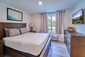 A bedroom with a bed, a nightstand, a dresser, a lamp, a TV, and a window with curtains. - The Ruby 203 (Pigeon Forge)