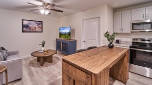 Una cocina moderna con una isla central, un área de comedor con una mesa redonda, un ventilador de techo y un televisor de pantalla plana montado.