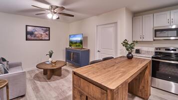 A modern kitchen with a central island, a dining area with a round table, a ceiling fan, and a mounted flat-screen TV.