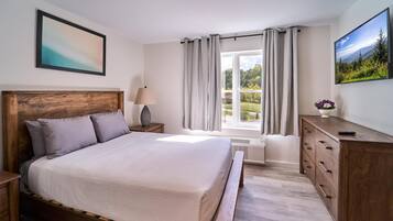 A bedroom with a wooden bed, a nightstand, a dresser, a window with curtains, and a painting on the wall.