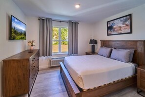 A bedroom with a bed, a nightstand, a dresser, a window with curtains, and a painting on the wall. - The Ruby 205 (Pigeon Forge)