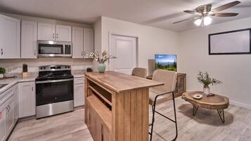 A modern kitchen with stainless steel appliances, a wooden island, and a dining area with a chair and table.