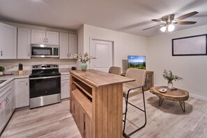 A modern kitchen with stainless steel appliances, a wooden island, and a dining area with a chair and table. - The Ruby 205 (Pigeon Forge)