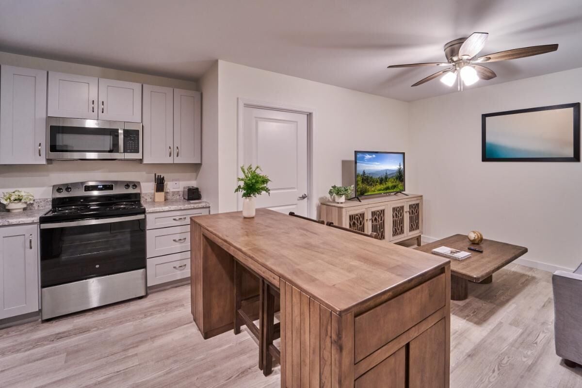A modern kitchen with stainless steel appliances, a wooden dining table, and a ceiling fan.