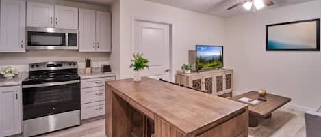 A modern kitchen with stainless steel appliances, a wooden dining table, and a ceiling fan.