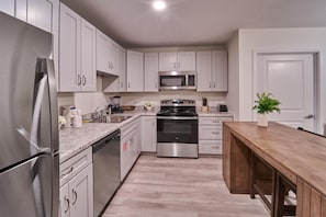 A modern kitchen with stainless steel appliances, white cabinetry, and a wooden dining table. - The Ruby 206 (Pigeon Forge)