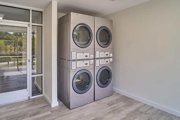 A laundry room with four stacked front-loading washing machines, a glass door leading to an outdoor area, and a wooden floor. - The Ruby 206 (Pigeon Forge)