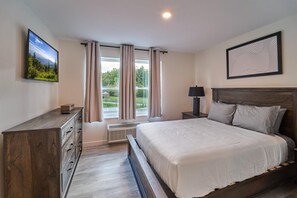 A bedroom with a bed, a TV, a dresser, a window with curtains, and a framed picture on the wall. - The Ruby 206 (Pigeon Forge)