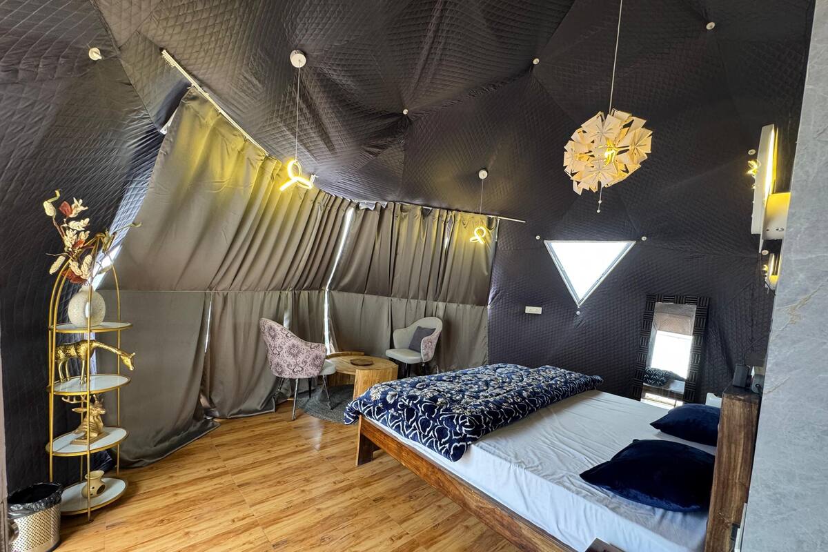 Une pièce aménagée comme une tente, avec un lit, deux chaises, une petite table et un luminaire suspendu.