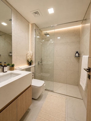 Un baño moderno con cabina de ducha de vidrio, inodoro, lavamanos con espejo y una pequeña planta en maceta.
