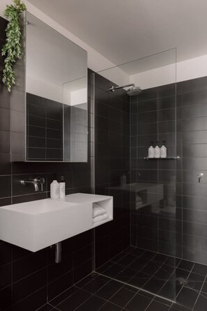 A modern bathroom with a glass shower enclosure, a white sink, and a mirror above it. - 2BD | Immaculate SkyHigh Apartment |Prime Location (Southbank)