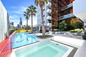A rooftop pool area with a view of the city skyline, palm trees, and modern buildings. - 2BD | Immaculate SkyHigh Apartment |Prime Location (Southbank)