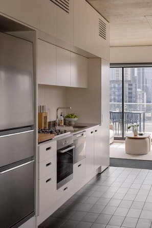A modern kitchen with stainless steel appliances, a built-in oven, and a large window overlooking a cityscape. - 2BD | Immaculate SkyHigh Apartment |Prime Location (Southbank)
