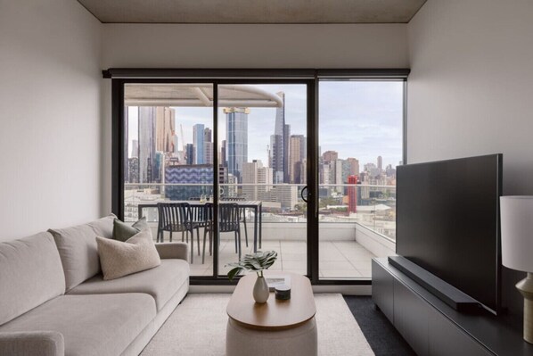 A modern living room with a sofa, coffee table, TV, and a balcony with a city view. - 2BD | Immaculate SkyHigh Apartment |Prime Location (Southbank)