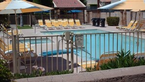 A swimming pool with sun loungers and umbrellas, a fenced area, and a sign indicating pool hours. - two bedrooms, two bathrooms, a full kitchen, living and dining areas. (Palm Springs)