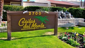 A sign for 'Casitas del Monte' with a palm tree graphic, a number '2700', and a landscaped garden with flowers and a stone feature. - two bedrooms, two bathrooms, a full kitchen, living and dining areas. (Palm Springs)