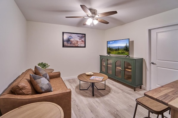 A living room with a sofa, a coffee table, a cabinet, a television, and a ceiling fan. - The Ruby 207 (Pigeon Forge)