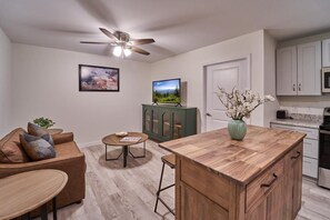 Eine moderne Küche mit einer Holztischinsel, Deckenventilator, Fernseher und Essbereich mit einer Couch und einem kleinen Tisch.