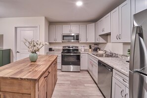 A modern kitchen with white cabinets, stainless steel appliances, a wooden island, and a vase of flowers. - The Ruby 207 (Pigeon Forge)