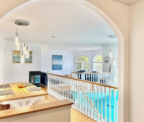 A spacious living area with a wooden dining table, a fireplace, and a view of a swimming pool through an arched doorway.