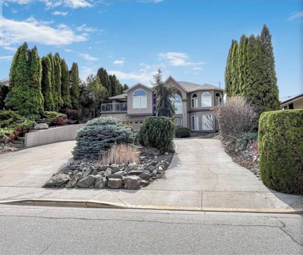 Une maison à deux étages avec une allée menant à la porte d’entrée, entourée d’un jardin bien entretenu et de grands arbres.