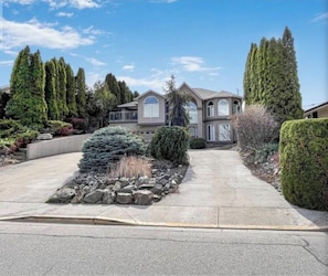 A two-story house with a driveway leading to the front door, surrounded by well-maintained landscaping and tall trees.