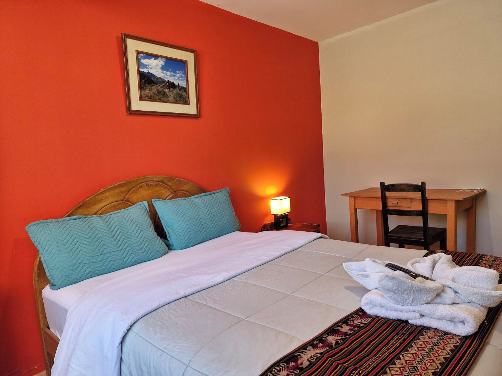 Una habitación de hotel con una cama, un escritorio, una silla, una lámpara y un cuadro en la pared.