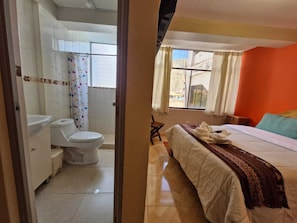 Un dormitorio con cama, ventana con cortinas y baño con inodoro y lavamanos.