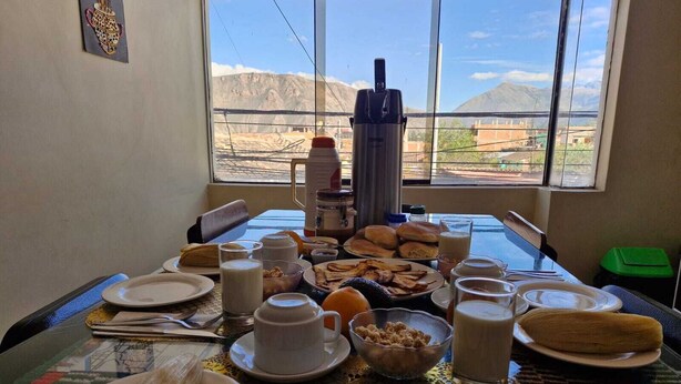 Een ontbijttafel met borden, melk, gebak, een koffiezetapparaat en een uitzicht op bergen door een raam.
