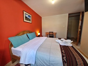 Un dormitorio con cama, mesita de noche, silla, puerta y un cuadro en la pared.
