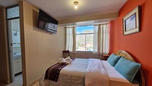 Een slaapkamer met een bed, een aan de muur bevestigde televisie, een raam met gordijnen en uitzicht op buiten.