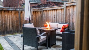 Un patio con mobiliario de mimbre, una fogata y una valla de madera.