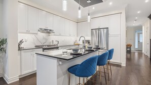 Una cucina moderna con mobili bianchi, elettrodomestici in acciaio inossidabile e un'isola centrale con sgabelli da bar.