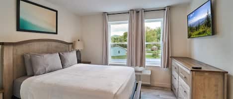 Ein Schlafzimmer mit Bett, Schminktisch, einem Fenster mit Vorhängen und einem Gemälde an der Wand.