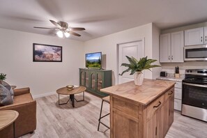 A modern kitchen with a central island, a dining area with a round table, a ceiling fan, and a green cabinet. - The Ruby 208 (Pigeon Forge)