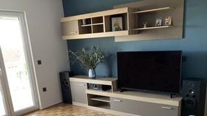 Un salon avec un téléviseur, des meubles en bois, un canapé à motifs floraux et un parquet en chevrons.