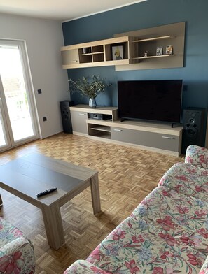 A living room with a TV, wooden furniture, a floral sofa, and a herringbone floor. - Vacation apartment in Montenegro. Quiet location near the sea. Welcome! (Bar)