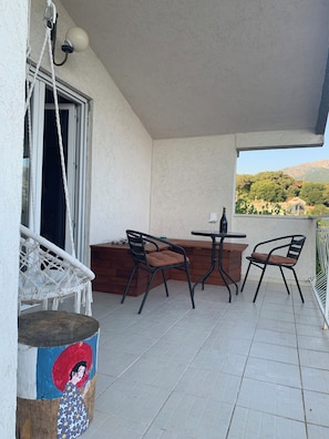 A balcony with a table and chairs, a hanging chair, and a view of the landscape. - Vacation apartment in Montenegro. Quiet location near the sea. Welcome! (Bar)